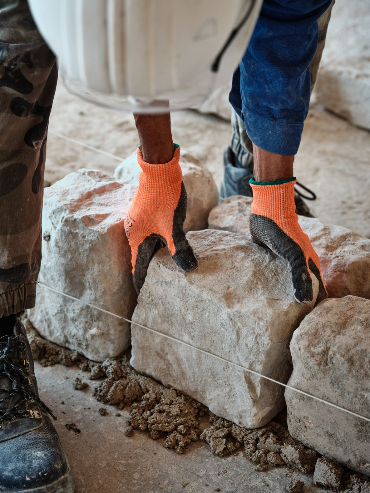 Focus sur le geste d'un ouvrier posant une pierre sur le chantier.